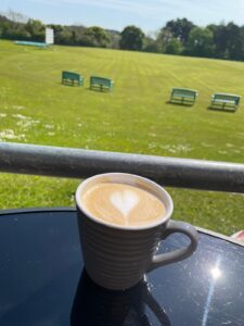 A photo of a lovely cup of coffee with a view of the cricket pitch on a sunny day
